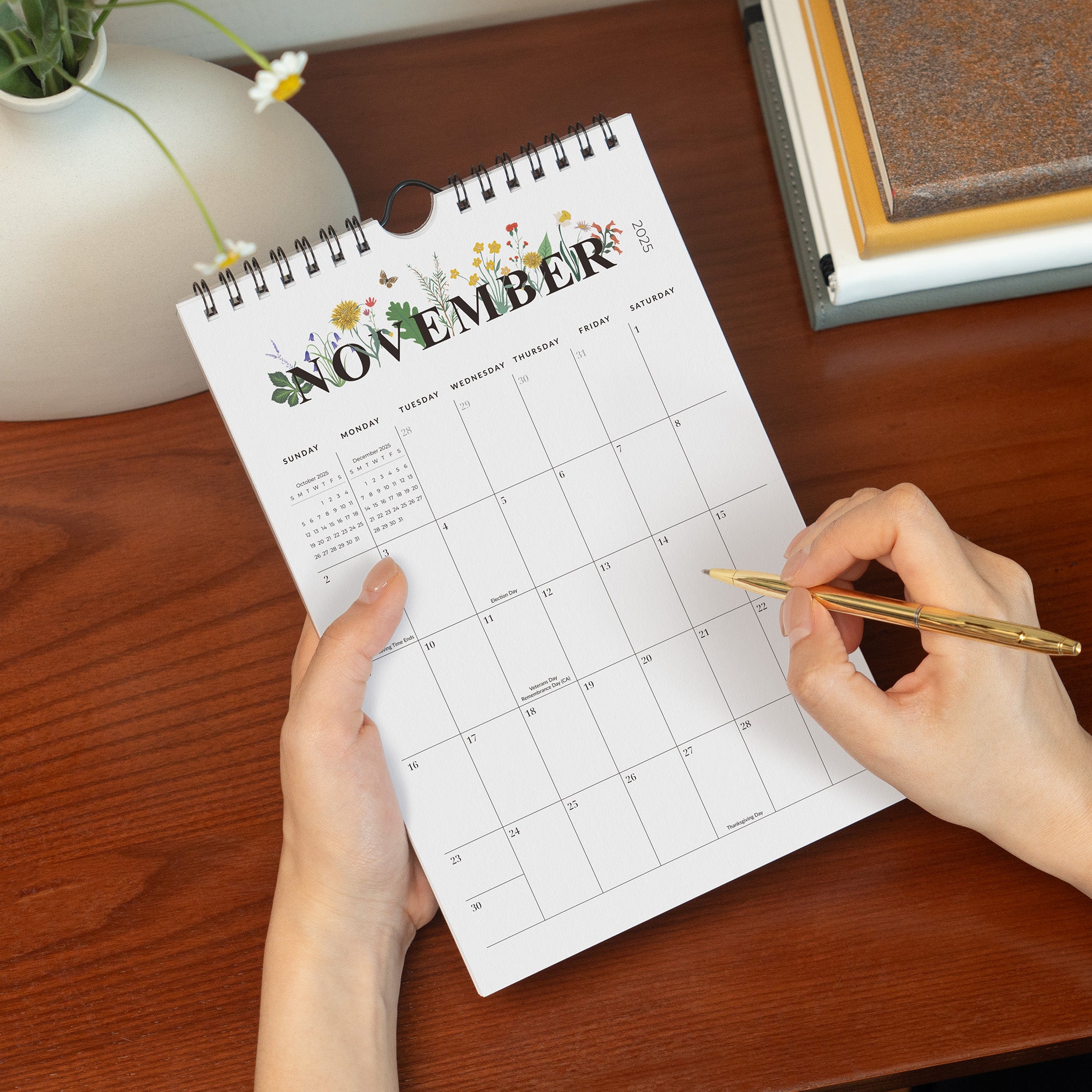 Person holding a November calendar with a pen on a wooden surface.